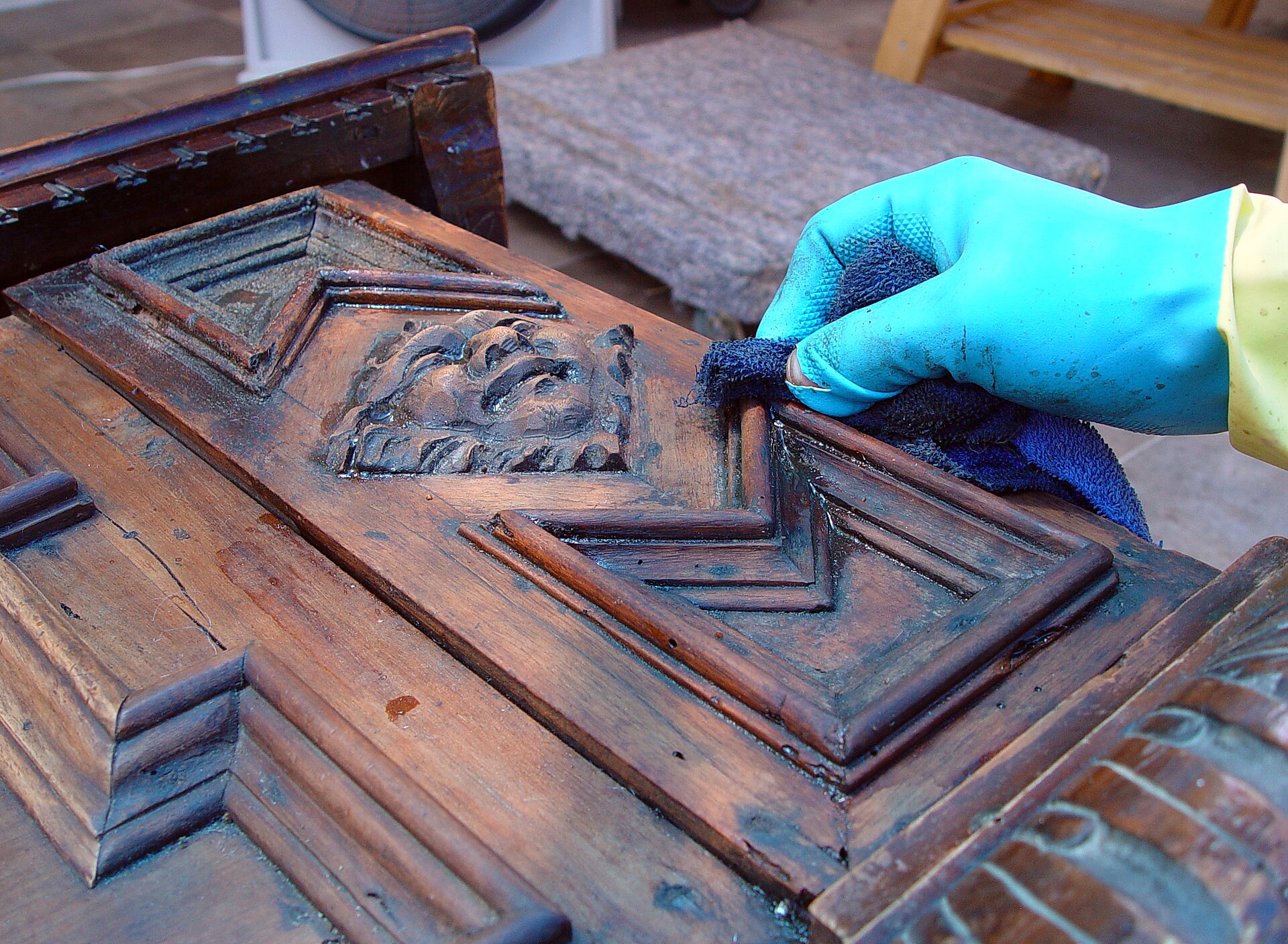 Gloved conservator applying paint remover to carved wooden furniture