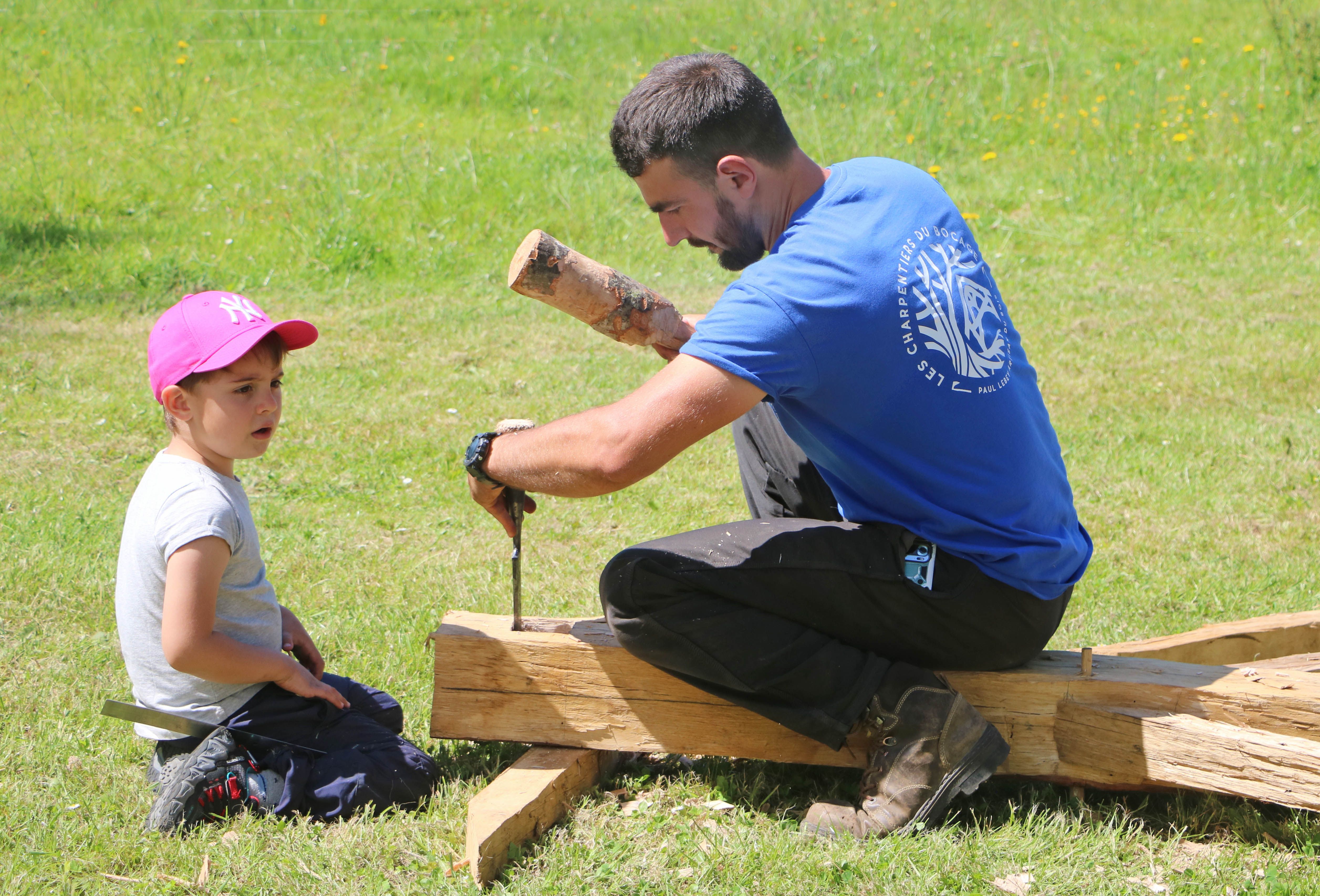 Adult using a hand tool on timber while a child watches from beside the work area