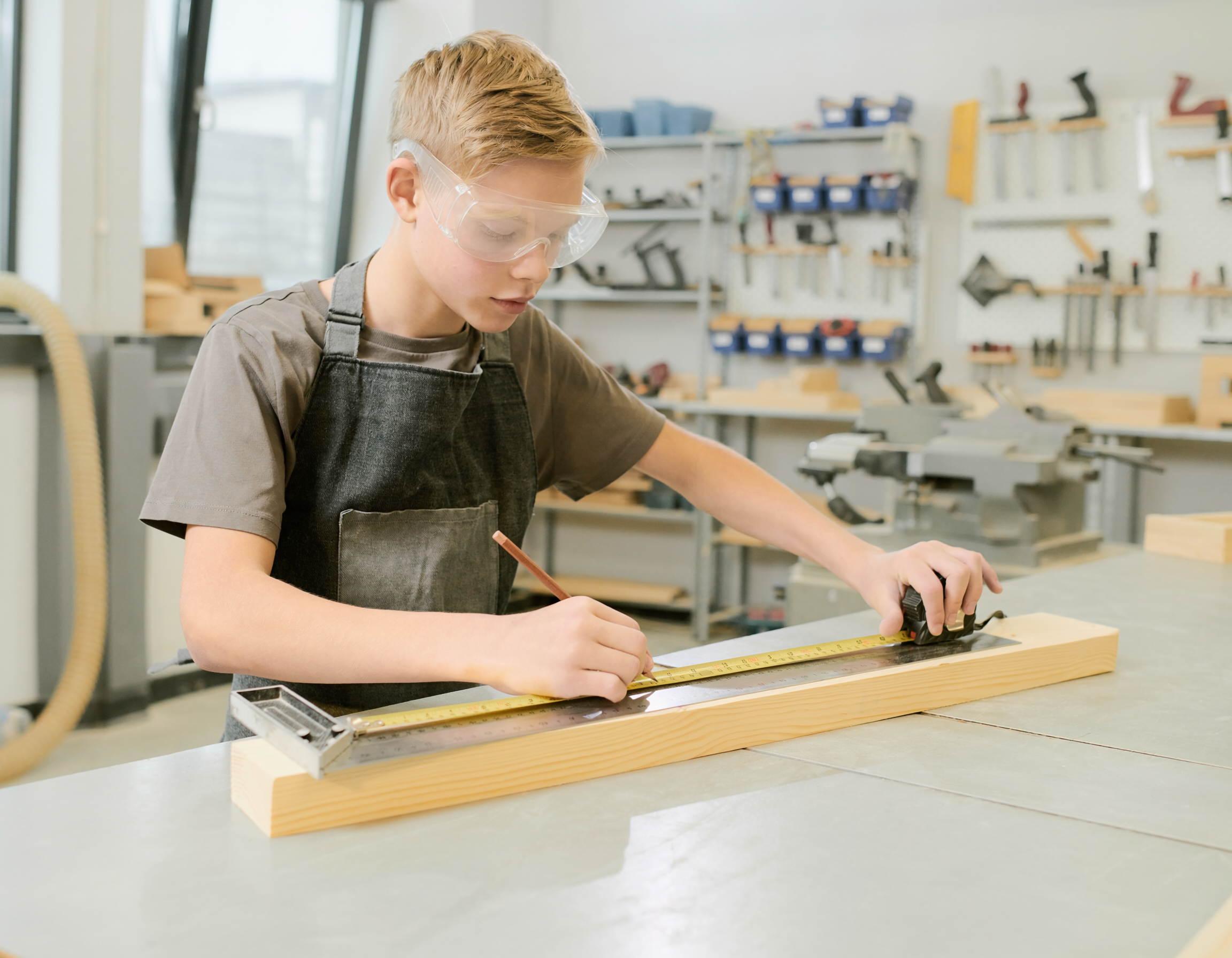 Young maker measuring and marking a board at a woodworking bench